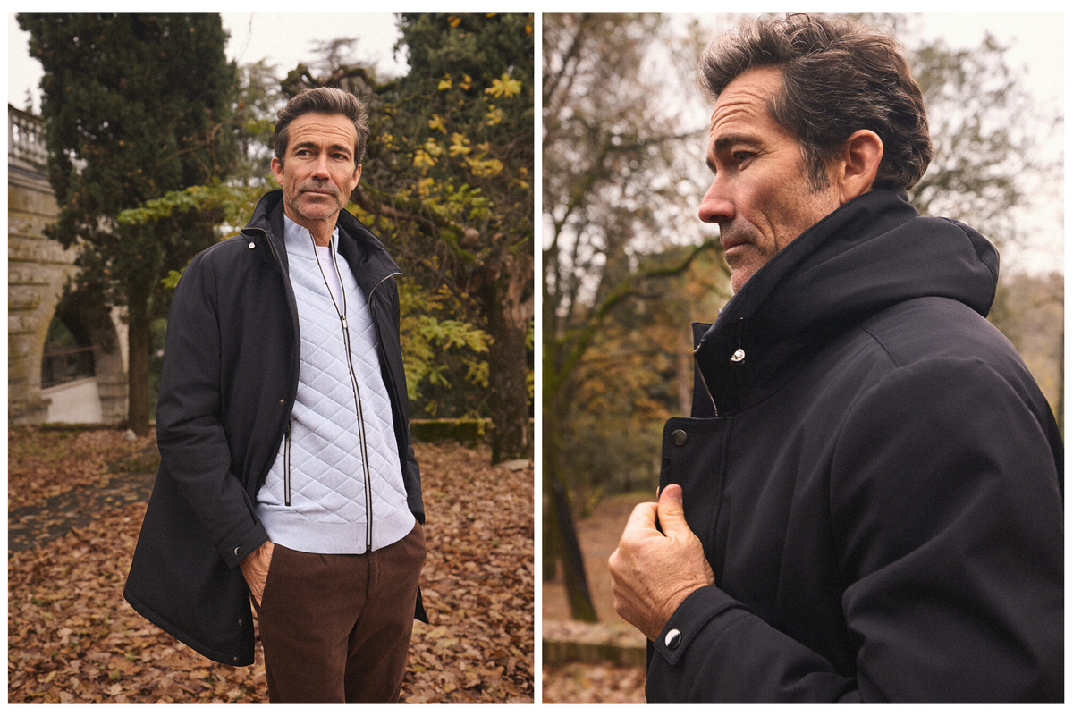 Άνδρας με μαύρο παλτό και καπιτονέ γαλάζιο jacket στέκεται στο Roncolo, ανάμεσα σε φθινοπωρινά φύλλα, στο πλαίσιο της καμπάνιας Portobello’s Fall–Winter 2026.